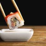chopsticks holding a sushi roll over a bowl of soy sauce
