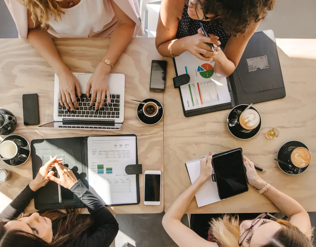 a group of women sitting around a table with laptops and coffee